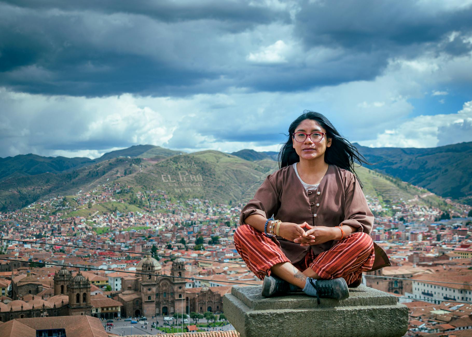 Podróżniczka na dachu z widokiem na zabudowę i wzgórza Cusco