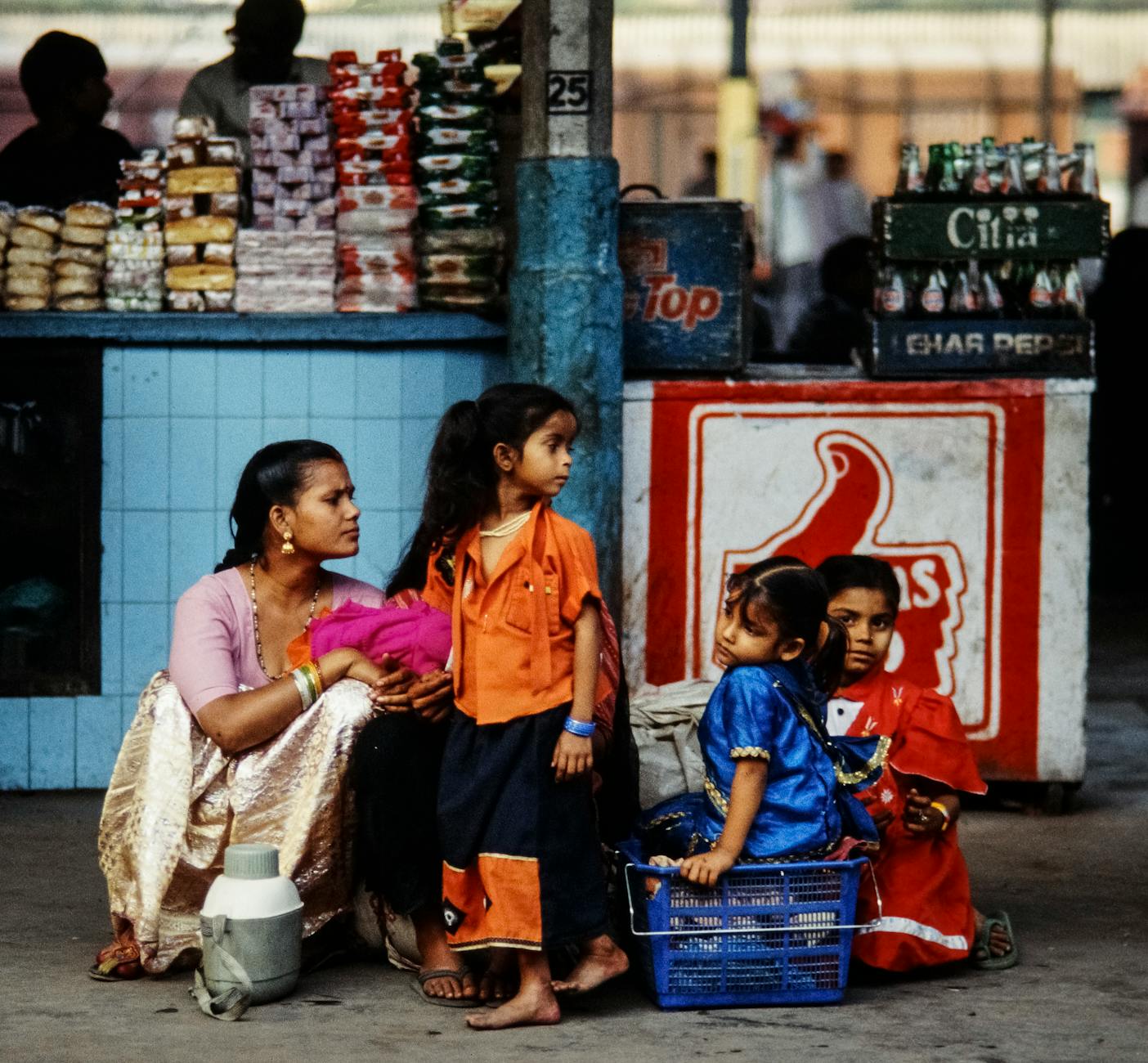 Rodzina z dziećmi czeka na pociąg przy straganie na dworcu w Indiach